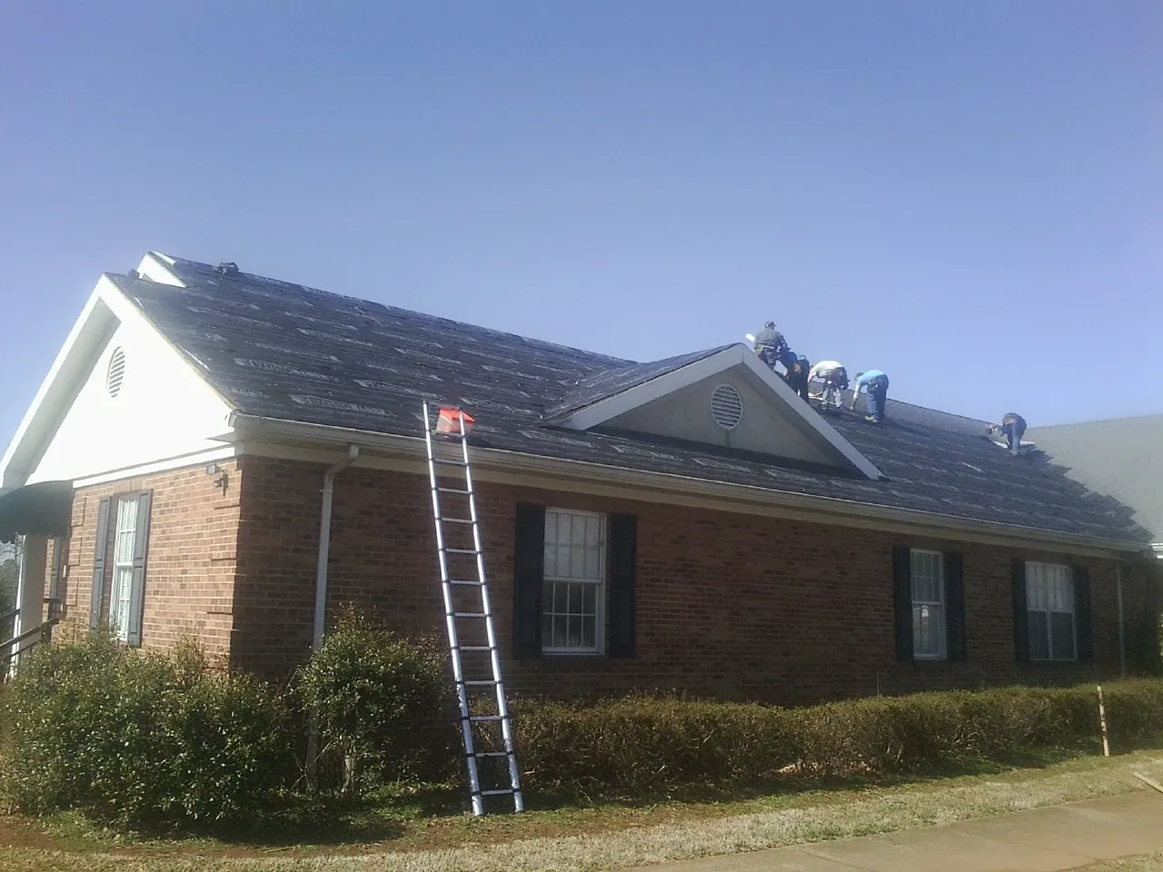 Crew tearing shingles off a brick ranch roof with a ladder set — Metal Roof Repair work by our crew in Jackson Center