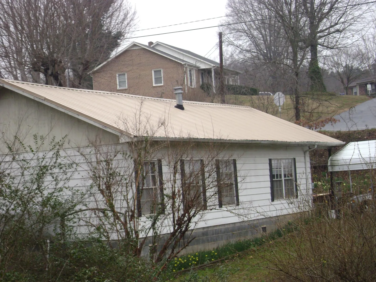 Tan metal roof on a white sided house set into a hillside — Commercial Roofing by Roofing Brothers in Jackson Center